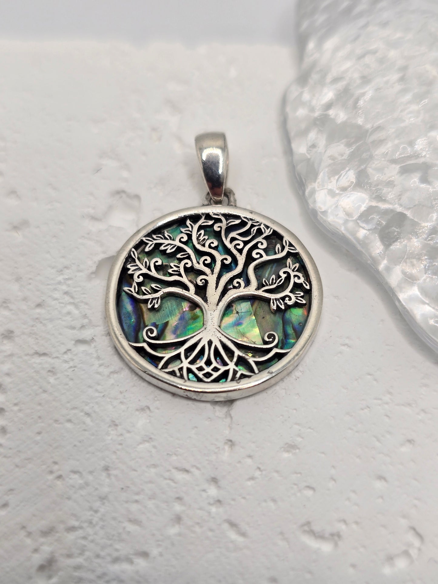 Celebrate growth, harmony, and connection with the Tree of Life Pendant, crafted in luminous 925 sterling silver and set over an iridescent abalone shell inlay. Sea-blue and green tones shimmer beneath finely detailed branches, evoking roots in nature and branches reaching toward the sky—a timeless emblem of renewal and balance.
Intricate silverwork forms swirling limbs that invite a closer look, while the natural shell backdrop ensures every piece has its own unique play of colour. Wear it daily as a symb