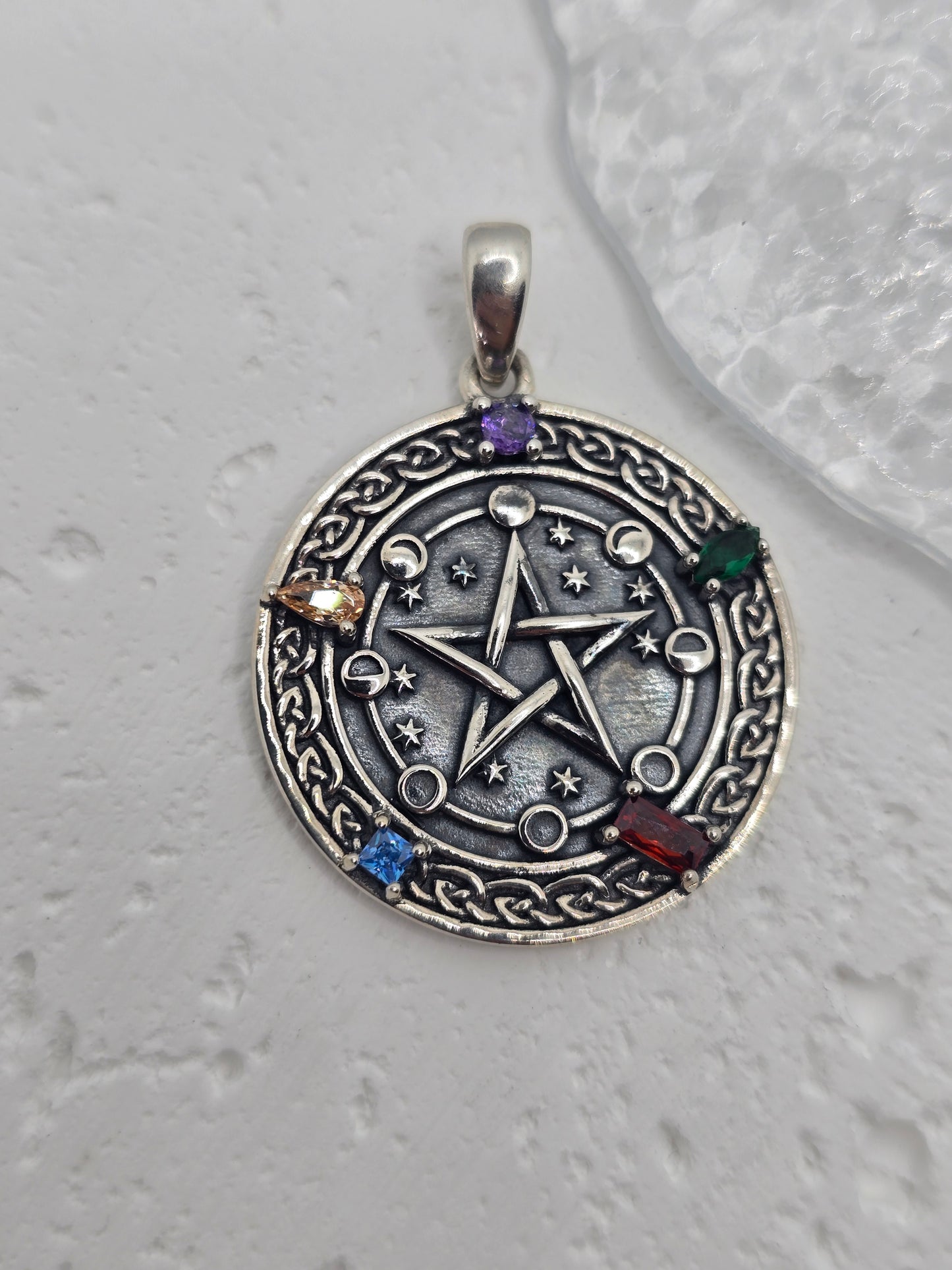 Unlock the power of cosmic energy and elemental balance with this Pentagram Cosmic Cycle Amulet, beautifully crafted from 925 sterling silver and set with vibrant chakra gemstones. This mystical pendant merges the ancient power of the pentagram with the cyclical wisdom of the lunar phases, creating a talisman that protects, empowers, and aligns the spirit.
At the center lies a classic five-pointed star, long revered as a symbol of protection, spiritual knowledge, and harmony between the elements—earth, air