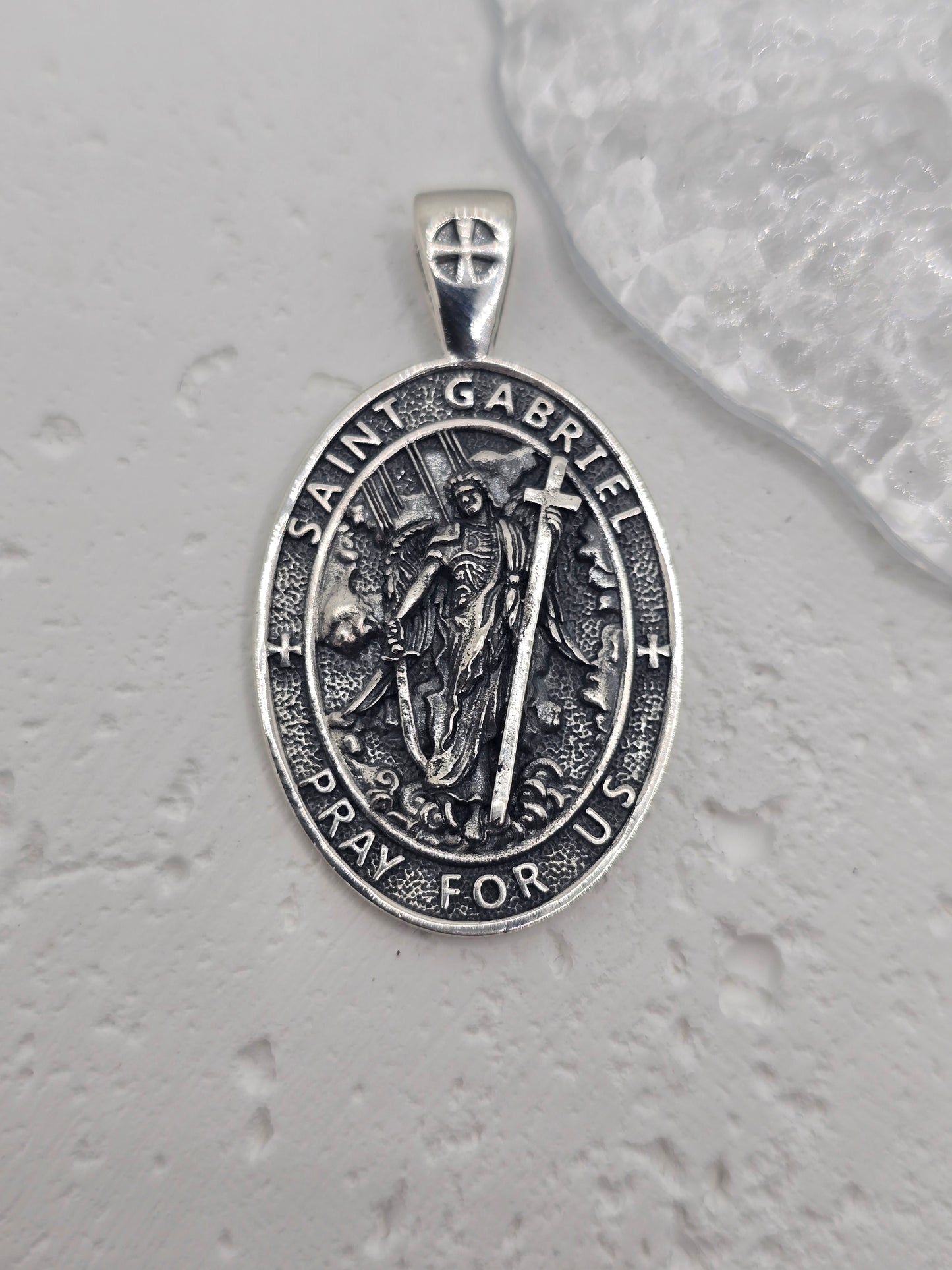 Embrace divine communication and protection with the St. Gabriel Amulet Pendant, crafted in luminous 925 sterling silver. Revered across faith traditions as the messenger of God, Archangel Gabriel is beautifully depicted on this pendant, offering guidance, clarity, and spiritual reassurance to those who wear it.
Known for delivering messages of hope and truth, Gabriel is shown with delicately detailed wings, poised in celestial grace. Surrounding the image is the inscription: "Pray for Us"—a quiet invocati