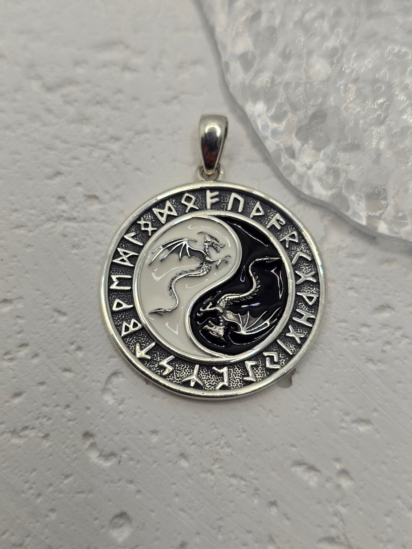 This Yin Yang Dragon Pendant, crafted in 925 sterling silver, is a powerful fusion of Eastern philosophy and Norse runic tradition. At its center lies the iconic Yin Yang symbol, each half inhabited by a detailed dragon—one representing Yang (light, action, masculine), the other Yin (darkness, stillness, feminine). Together, they embody the eternal dance of balance, duality, and harmony.
Surrounding the dragons is a ring of ancient Norse runes, weaving another layer of meaning—protection, knowledge, and th