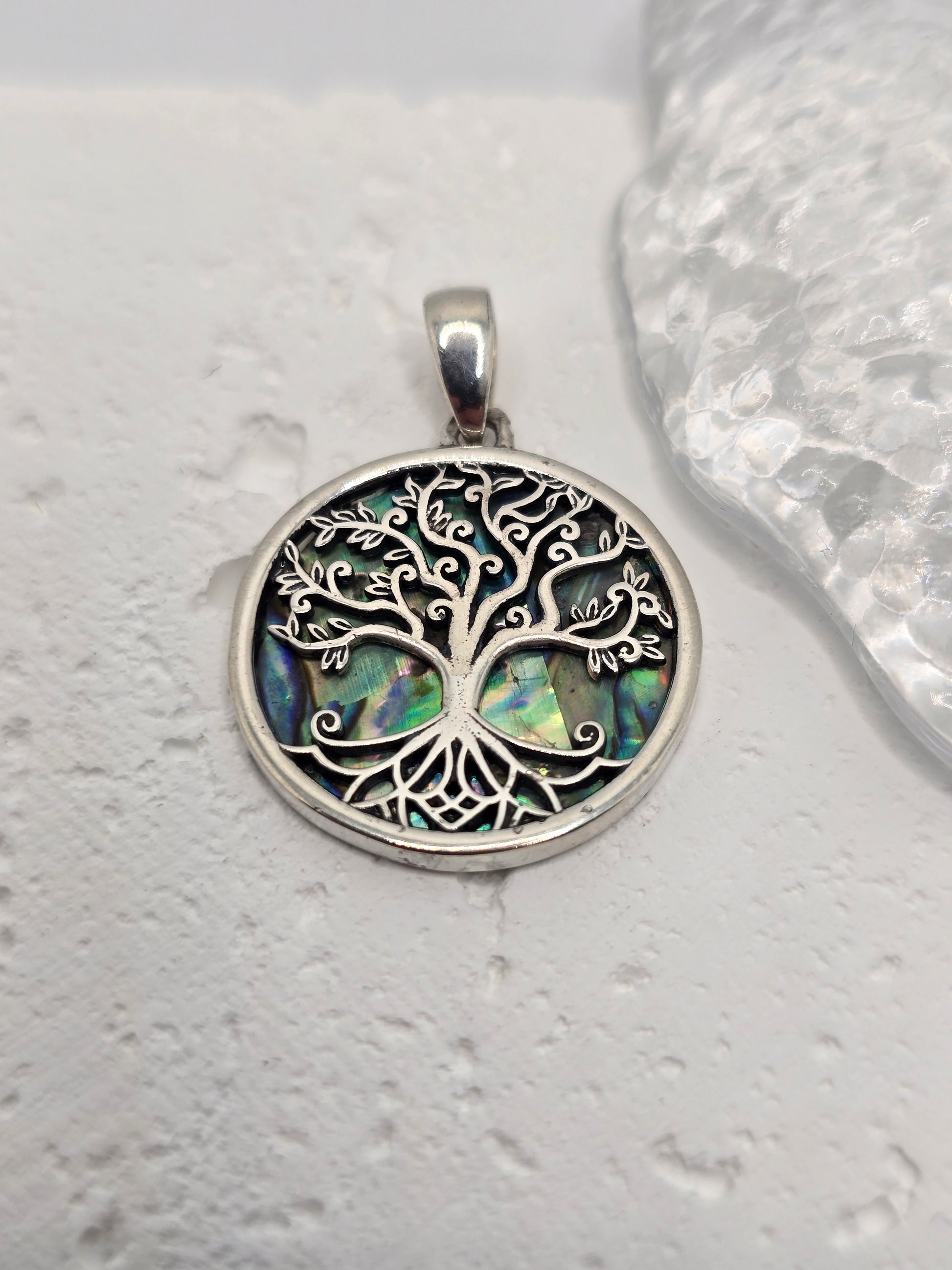 Celebrate growth, harmony, and connection with the Tree of Life Pendant, crafted in luminous 925 sterling silver and set over an iridescent abalone shell inlay. Sea-blue and green tones shimmer beneath finely detailed branches, evoking roots in nature and branches reaching toward the sky—a timeless emblem of renewal and balance.

Intricate silverwork forms swirling limbs that invite a closer look, while the natural shell backdrop ensures every piece has its own unique play of colour. Wear it daily as a symb