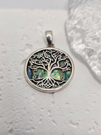 Celebrate growth, harmony, and connection with the Tree of Life Pendant, crafted in luminous 925 sterling silver and set over an iridescent abalone shell inlay. Sea-blue and green tones shimmer beneath finely detailed branches, evoking roots in nature and branches reaching toward the sky—a timeless emblem of renewal and balance.

Intricate silverwork forms swirling limbs that invite a closer look, while the natural shell backdrop ensures every piece has its own unique play of colour. Wear it daily as a symb