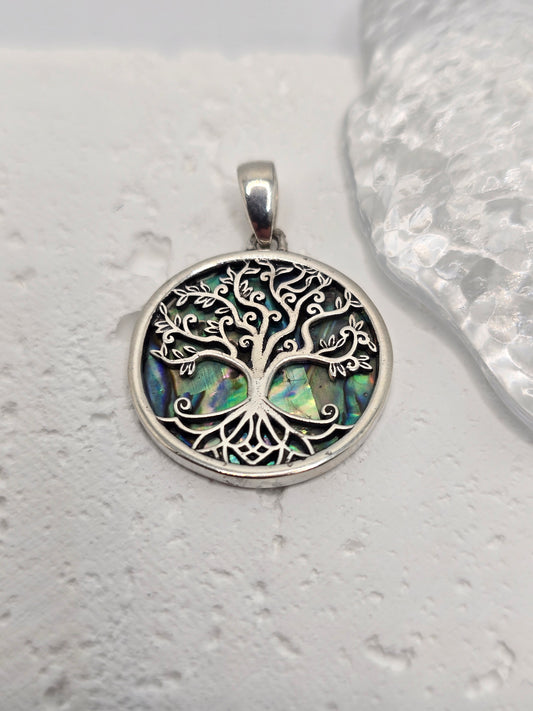 Celebrate growth, harmony, and connection with the Tree of Life Pendant, crafted in luminous 925 sterling silver and set over an iridescent abalone shell inlay. Sea-blue and green tones shimmer beneath finely detailed branches, evoking roots in nature and branches reaching toward the sky—a timeless emblem of renewal and balance.

Intricate silverwork forms swirling limbs that invite a closer look, while the natural shell backdrop ensures every piece has its own unique play of colour. Wear it daily as a symb