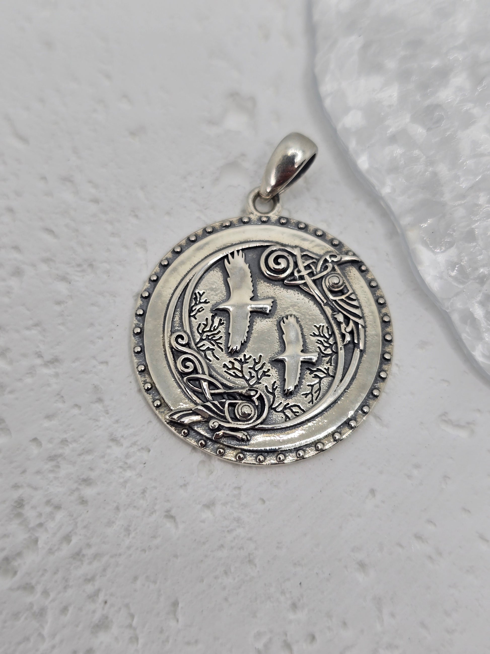Step into the mystic shadows of the ancient forest with this Viking Crow Medallion, forged from solid 925 sterling silver and brought to life with deep symbolism and fine detail. At the heart of the design stand Huginn and Muninn, Odin’s trusted ravens, surrounded by an enchanted woodland scene carved into silver—a tribute to Norse mythology and the pursuit of knowledge.

Encircling the forest and birds is a ring of Norse runes, each symbol a whisper of ancient magic, representing insight, wisdom, and the u