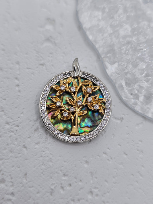 Celebrate the wonder of life with this radiant Tree of Life Charm Pendant, crafted in 925 sterling silver and highlighted with a warm gold-tone finish. At its center stands the Tree of Life, a timeless symbol of connection, growth, and grounding—each branch and leaf finely detailed and kissed with sparkling clear crystals, like sunlight catching the morning dew.

Behind the tree lies a stunning abalone shell backdrop, swirling with iridescent oceanic hues—a vivid reminder of nature’s beauty and life’s ever-