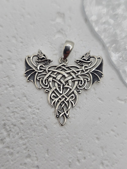 Step into the realm of legend with this Twin Dragons Pendant, crafted from solid 925 sterling silver and steeped in the ancient spirit of Celtic myth and romance. Two dragons, symbols of strength and loyalty, curl around one another in perfect symmetry, their entwined forms shaping a heart—representing love, unity, and unbreakable bonds.

Framing the dragons is intricate Celtic knotwork, a pattern without beginning or end, reflecting the eternal cycles of life and the enduring nature of love and connection.