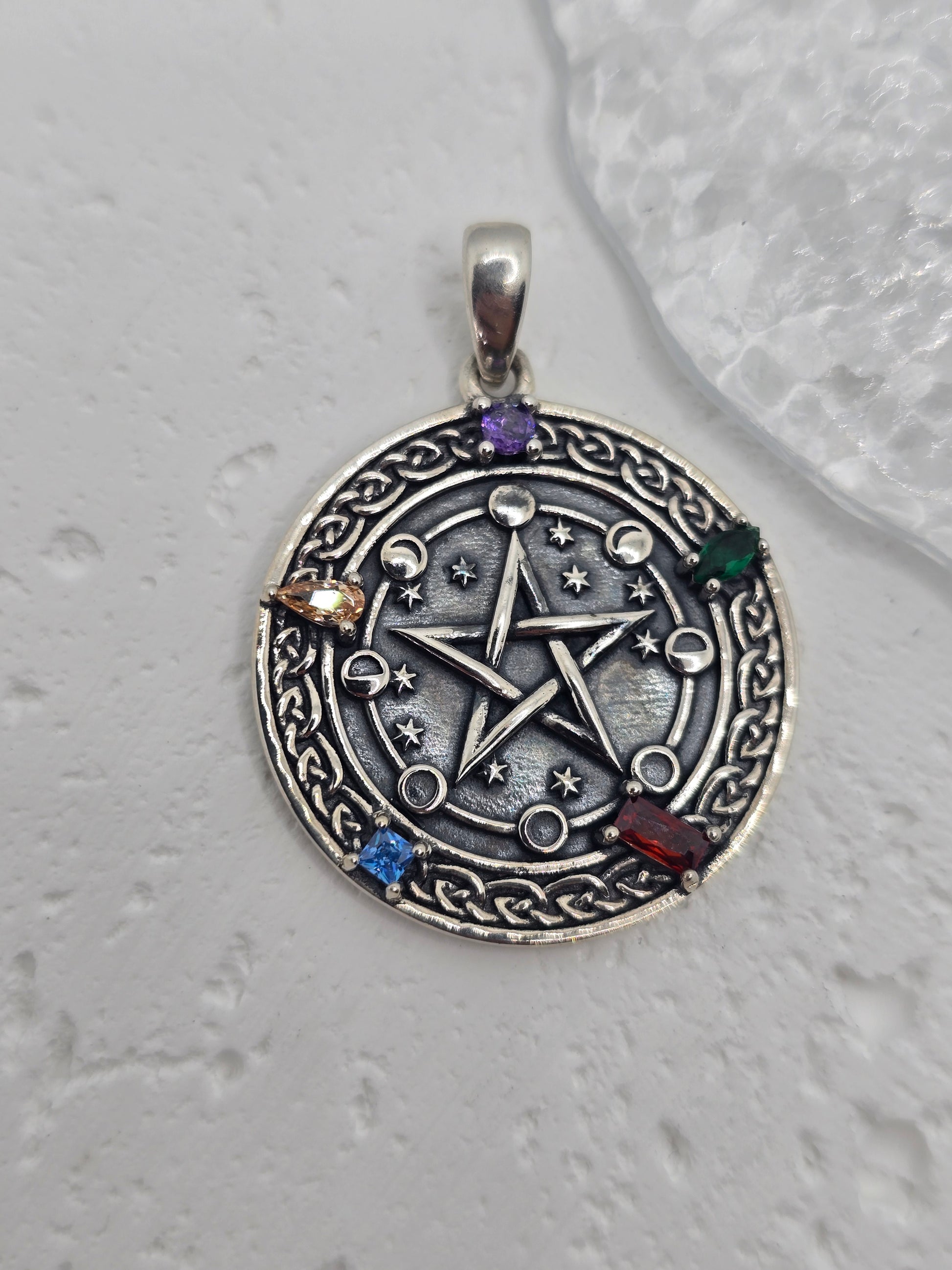 Unlock the power of cosmic energy and elemental balance with this Pentagram Cosmic Cycle Amulet, beautifully crafted from 925 sterling silver and set with vibrant chakra gemstones. This mystical pendant merges the ancient power of the pentagram with the cyclical wisdom of the lunar phases, creating a talisman that protects, empowers, and aligns the spirit.

At the center lies a classic five-pointed star, long revered as a symbol of protection, spiritual knowledge, and harmony between the elements—earth, air
