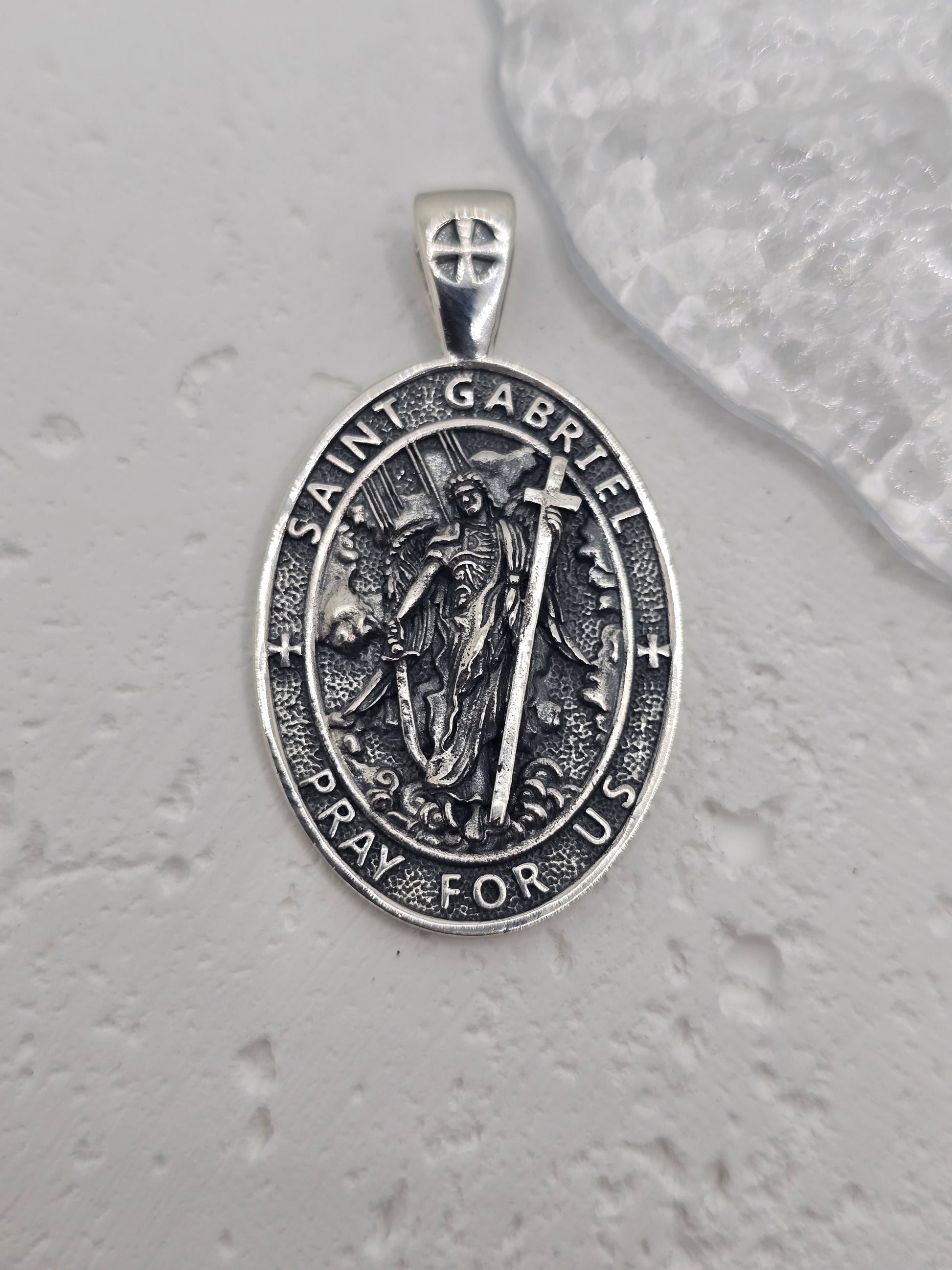 Embrace divine communication and protection with the St. Gabriel Amulet Pendant, crafted in luminous 925 sterling silver. Revered across faith traditions as the messenger of God, Archangel Gabriel is beautifully depicted on this pendant, offering guidance, clarity, and spiritual reassurance to those who wear it.

Known for delivering messages of hope and truth, Gabriel is shown with delicately detailed wings, poised in celestial grace. Surrounding the image is the inscription: "Pray for Us"—a quiet invocati