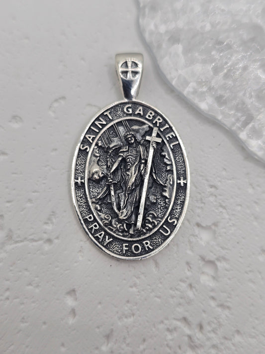 Embrace divine communication and protection with the St. Gabriel Amulet Pendant, crafted in luminous 925 sterling silver. Revered across faith traditions as the messenger of God, Archangel Gabriel is beautifully depicted on this pendant, offering guidance, clarity, and spiritual reassurance to those who wear it.

Known for delivering messages of hope and truth, Gabriel is shown with delicately detailed wings, poised in celestial grace. Surrounding the image is the inscription: "Pray for Us"—a quiet invocati