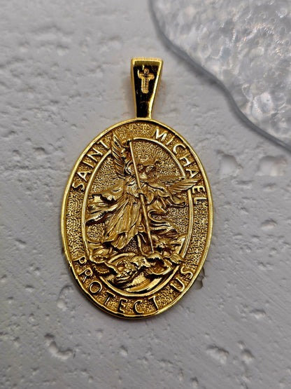 Saint Michael Protection in Precious Metal
Embrace courage and divine guardianship with the Saint Michael Protection Pendant, crafted in solid 925 sterling silver and finished with 18K gold plating. The high-relief image of Saint Michael the Archangel triumphing over evil is encircled by the invocation “Saint Michael Protect Us,” offering strength, justice, and reassurance in challenging times.

The reverse carries a devotional inscription affirming protection and faith, adding spiritual depth to this elega