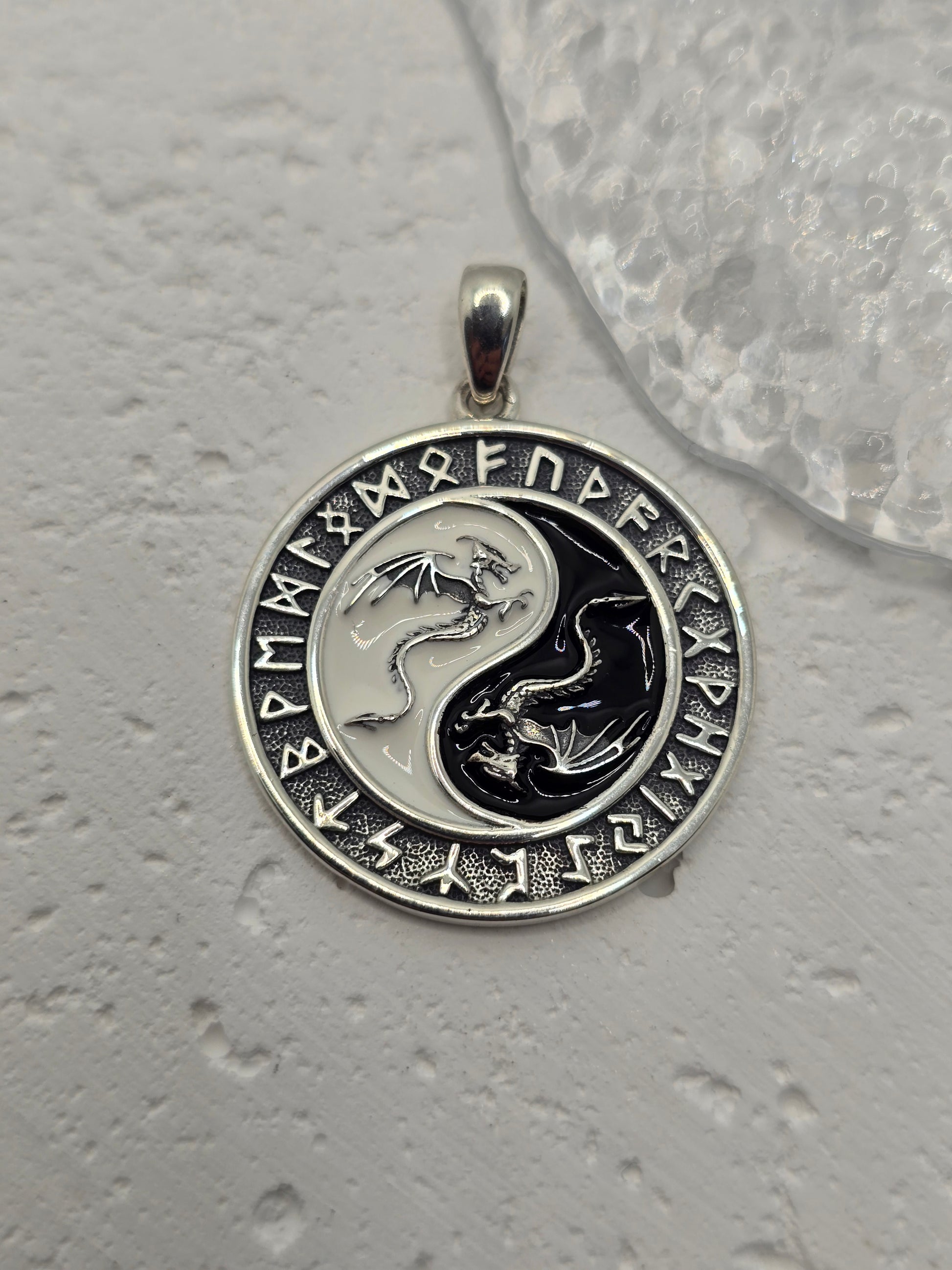 This Yin Yang Dragon Pendant, crafted in 925 sterling silver, is a powerful fusion of Eastern philosophy and Norse runic tradition. At its center lies the iconic Yin Yang symbol, each half inhabited by a detailed dragon—one representing Yang (light, action, masculine), the other Yin (darkness, stillness, feminine). Together, they embody the eternal dance of balance, duality, and harmony.

Surrounding the dragons is a ring of ancient Norse runes, weaving another layer of meaning—protection, knowledge, and th
