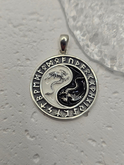 This Yin Yang Dragon Pendant, crafted in 925 sterling silver, is a powerful fusion of Eastern philosophy and Norse runic tradition. At its center lies the iconic Yin Yang symbol, each half inhabited by a detailed dragon—one representing Yang (light, action, masculine), the other Yin (darkness, stillness, feminine). Together, they embody the eternal dance of balance, duality, and harmony.

Surrounding the dragons is a ring of ancient Norse runes, weaving another layer of meaning—protection, knowledge, and th