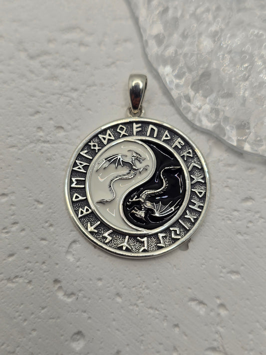 This Yin Yang Dragon Pendant, crafted in 925 sterling silver, is a powerful fusion of Eastern philosophy and Norse runic tradition. At its center lies the iconic Yin Yang symbol, each half inhabited by a detailed dragon—one representing Yang (light, action, masculine), the other Yin (darkness, stillness, feminine). Together, they embody the eternal dance of balance, duality, and harmony.

Surrounding the dragons is a ring of ancient Norse runes, weaving another layer of meaning—protection, knowledge, and th