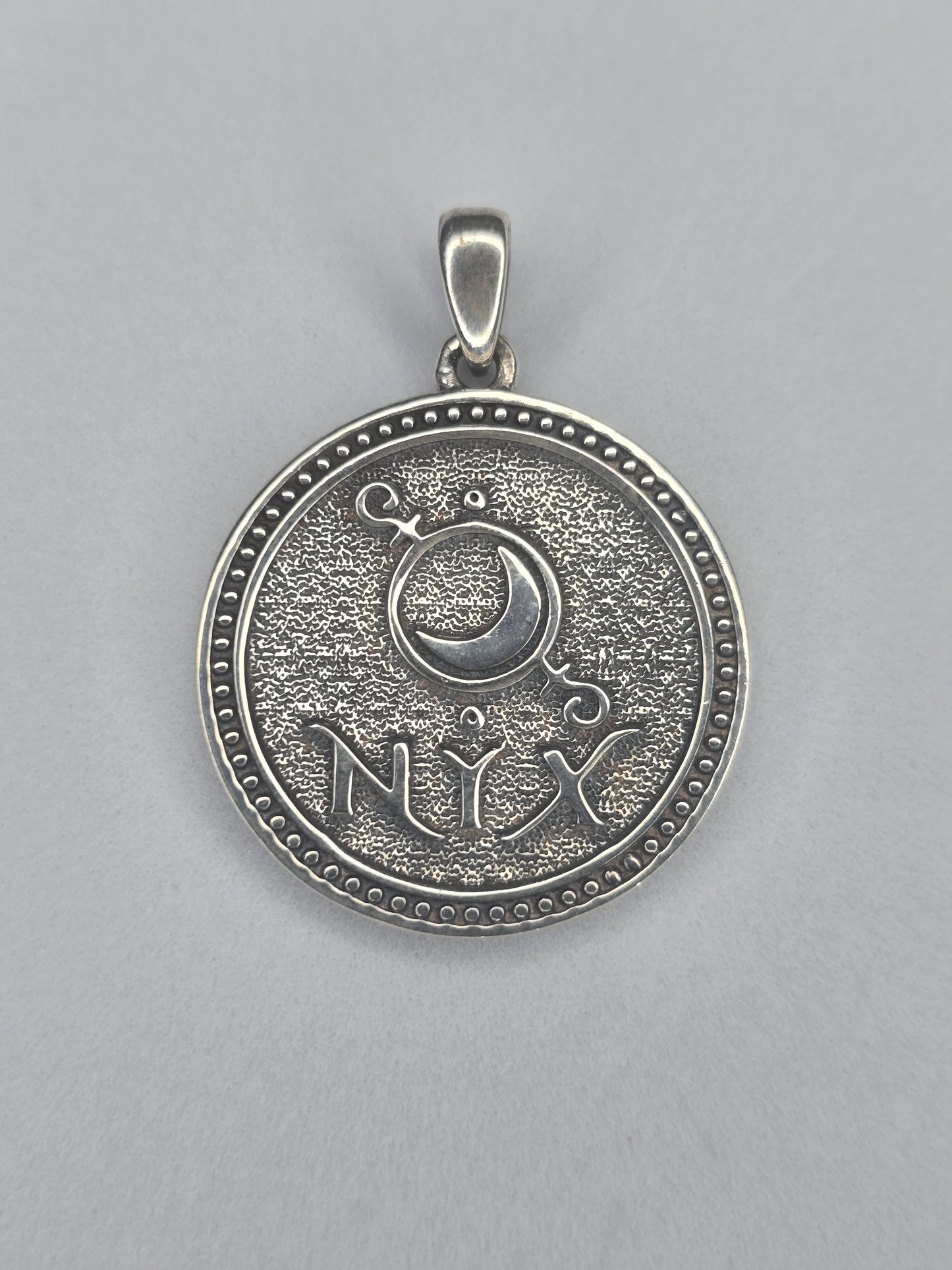 Back view of Nyx pendant with crescent moon symbol and NYX inscription in sterling silver