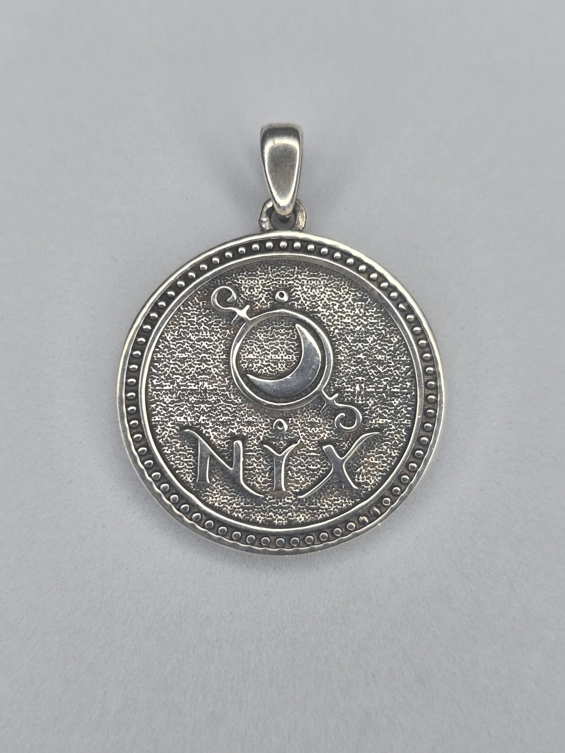 Back view of Nyx pendant with crescent moon symbol and NYX inscription in sterling silver